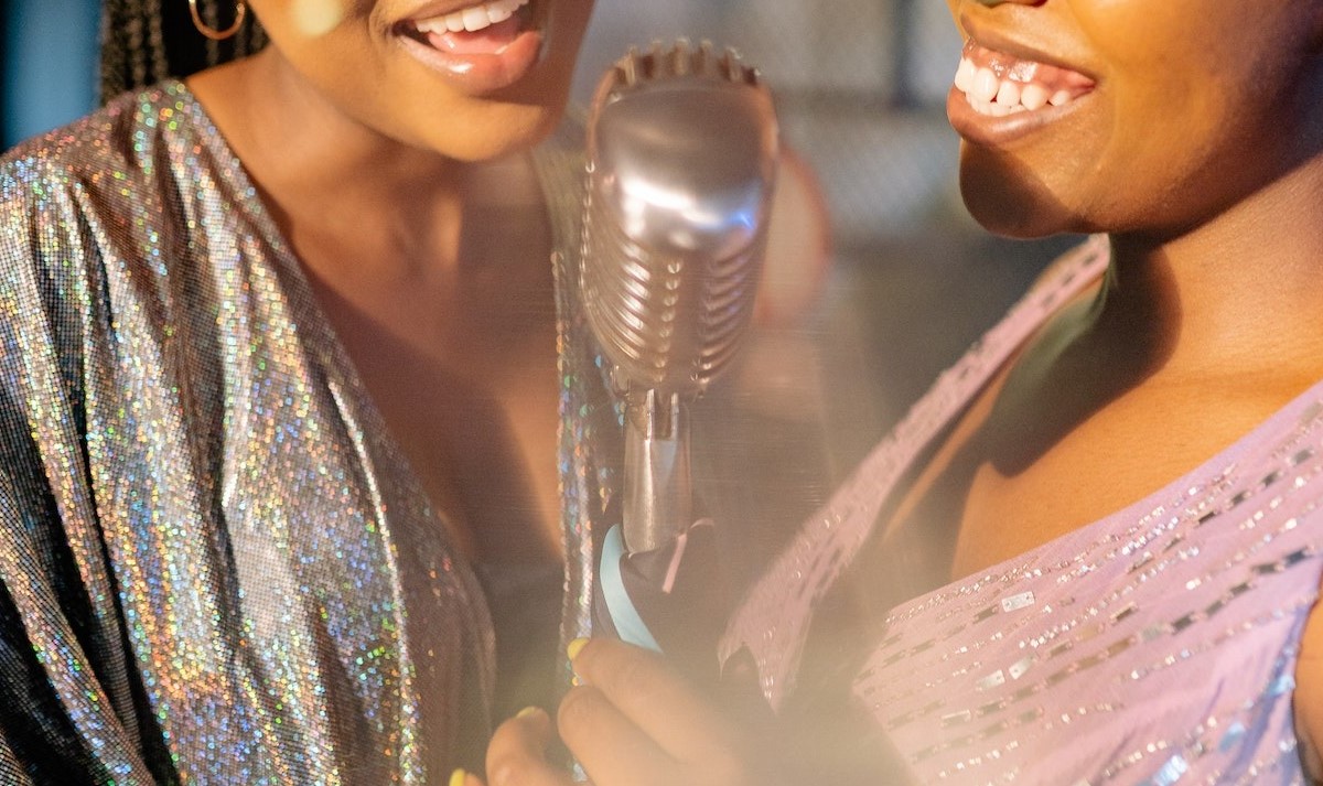 Closeup of two women singing a duet and holding a mic together